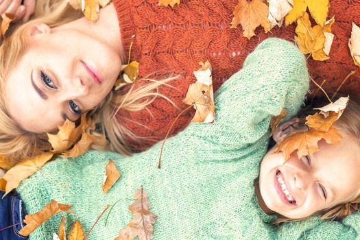 Little girl and young caucasian mom lying down directly above looking at camera on autumn leaves