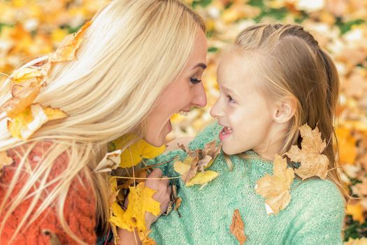 Beautiful young caucasian mother playing with her little child in the autumn park