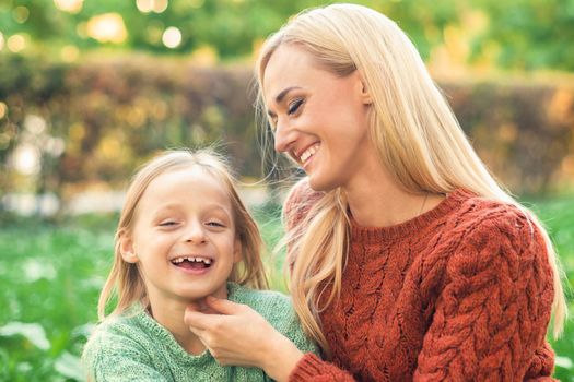 Beautiful young caucasian mother and little daughter smiling together on the green grass in the Autumn Park