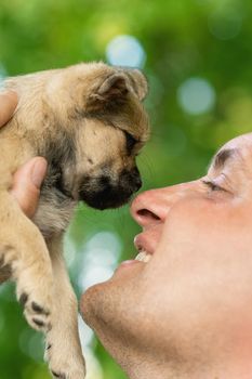 Happy young man looking at little cute puppy touching his nose outdoors