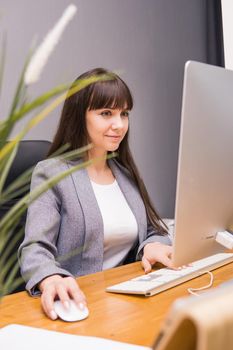 A brunette woman at a computer in the workplace. Business concept.