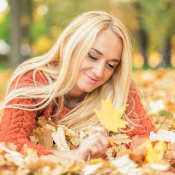 Beautiful young blond hair caucasian woman lies down on leaves at the autumn park
