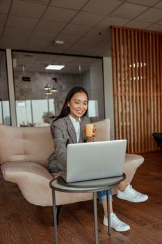Asian business woman working laptop and drink coffee sitting in cozy office. High quality photo