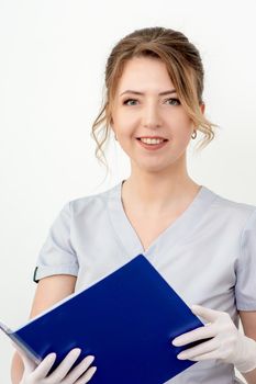 Portrait of beautiful young nurse holding blue folder in gloves looking at camera on white background