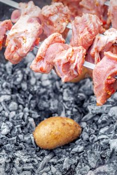 Hands of man prepares barbecue meat with potatoes on skewer by grill on fire outdoors. Concept of lifestyle rustic food preparation