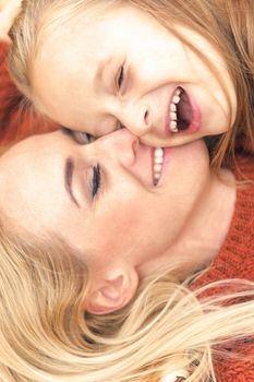 Little girl and young caucasian mom lying down directly above looking at camera on autumn leaves