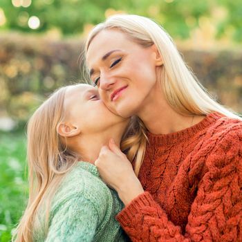 Cute daughter kisses her young mother while sitting at the park