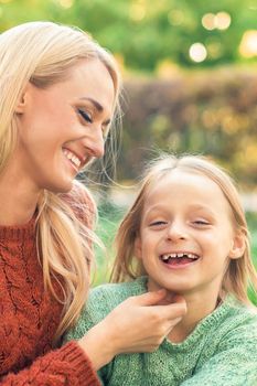 Beautiful young caucasian mother and little daughter smiling together on the green grass in the Autumn Park