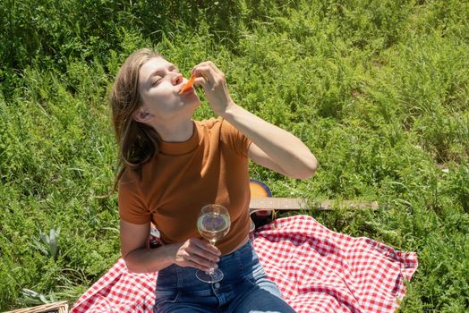 Young woman in park outside at sunny day, enjoying summertime dreaming and drinking wine. Millennial woman having picnic outdoors in sunny day