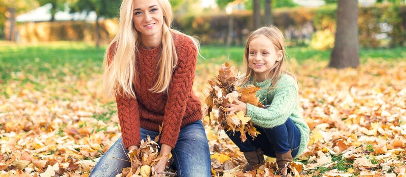 Happy young caucasian mother and little child playing with leaves in nature autumn park