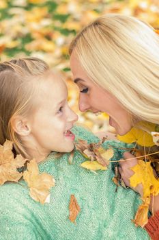 Beautiful young caucasian mother playing with her little child in the autumn park