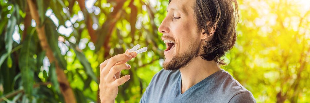 Man placing a bite plate in his mouth to protect his teeth at night from grinding caused by bruxism. BANNER, LONG FORMAT