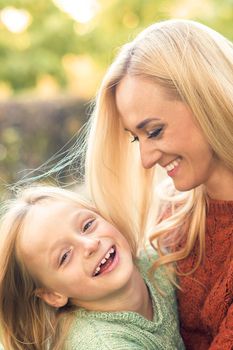 Beautiful young caucasian mother and little daughter smiling together on the green grass in the Autumn Park