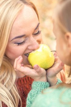 Portrait of little girl with young mother eating yellow apple in autumn park