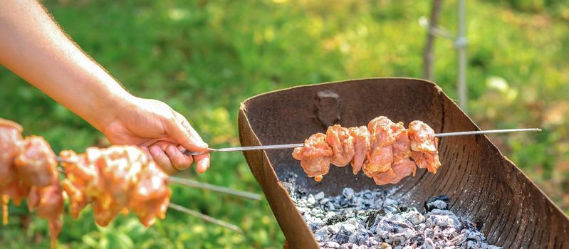 Hands of man prepares barbecue meat on skewer by grill on fire outdoors