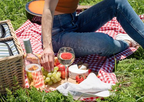 Young woman in park outside at sunny day, enjoying summertime dreaming and drinking wine. Millennial woman having picnic outdoors in sunny day