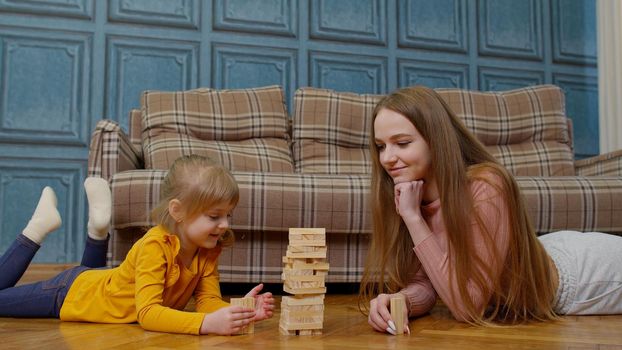 Mother play wooden blocks board game with little daughter child girl. Family enjoy comfort playtime together sit on floor in modern living room at home. Games for kid developmental, leisure hobbies