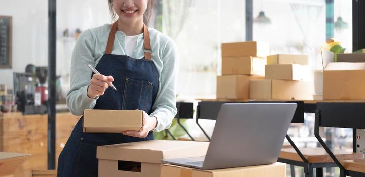 Shipping shopping online ,young start up small business owner writing address on cardboard box at workplace.small business entrepreneur SME or freelance asian woman working with box at home.