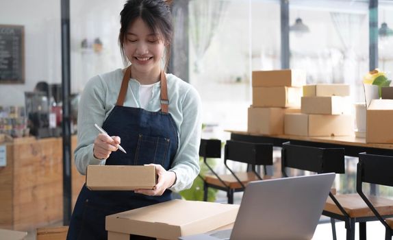 Shipping shopping online ,young start up small business owner writing address on cardboard box at workplace.small business entrepreneur SME or freelance asian woman working with box at home.