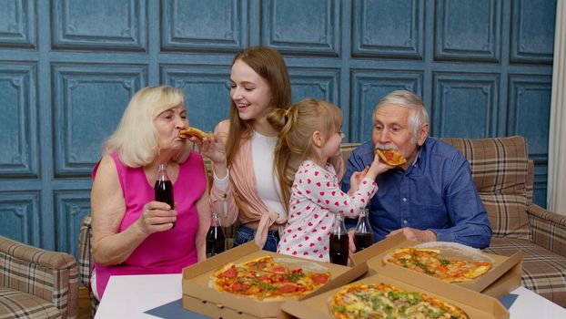 Multigenerational family having lunch party, feed each other with pizza, laughing, enjoying meal together at home. Grandparents with young woman and child. Celebration holidays, weekends, birthday