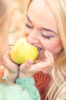 Portrait of little girl with young mother eating yellow apple in autumn park