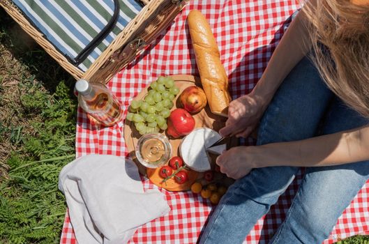 Young woman in park outside at sunny day, enjoying summertime dreaming and drinking wine. Millennial woman having picnic outdoors in sunny day