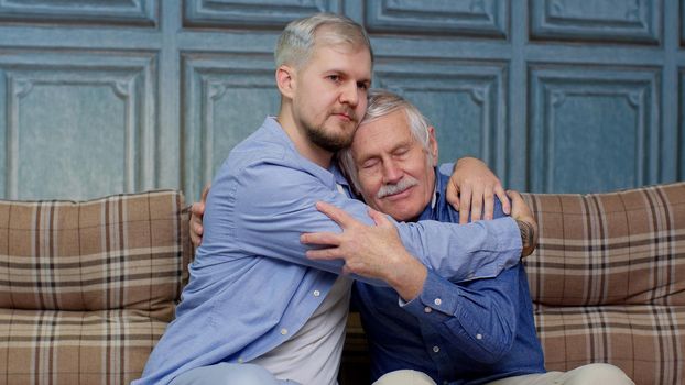Grown up son asking for apologizes to offended stressed elderly senior daddy, sitting together on couch. Compassionate young man supporting, giving psychological help to frustrated middle aged father.