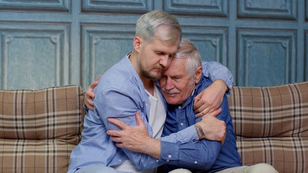 Handsome adult Caucasian man comforting his depressed senior father, asking about problems. Son hugging, consoling sadness old age dad with love. Mental health, healthcare and social problems concept