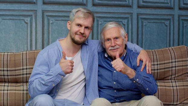 Cheerful excited young man with gray-haired old dad or grandfather. Joyful bonding loving different male generations family of senior father and handsome adult son or grandson showing thumb up gesture