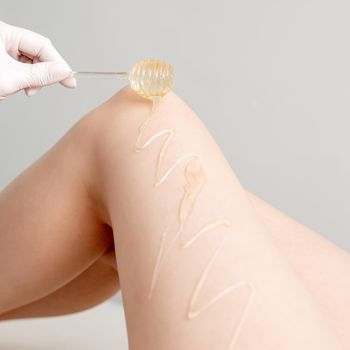 Wax on honey stick flowing down on female leg in human hand wearing protective glove on white background