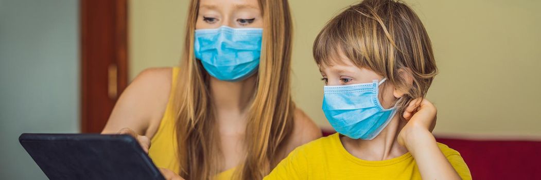 Boy studying online at home using a tablet. Mom helps him learn. Mom and son in medical masks to protect against coronovirus. Studying during quarantine. Global pandemic covid19 virus. BANNER, LONG FORMAT