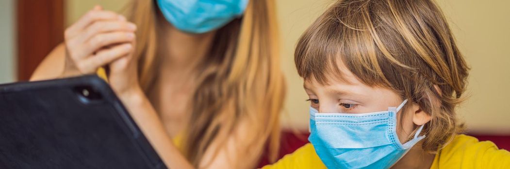Boy studying online at home using a tablet. Mom helps him learn. Mom and son in medical masks to protect against coronovirus. Studying during quarantine. Global pandemic covid19 virus. BANNER, LONG FORMAT