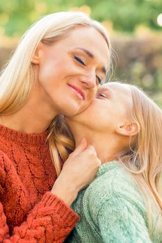 Cute daughter kisses her young mother while sitting at the park