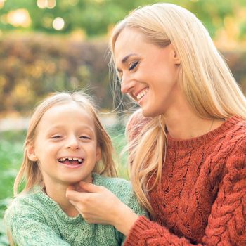 Beautiful young caucasian mother and little daughter smiling together on the green grass in the Autumn Park