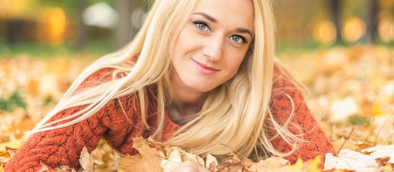 Beautiful young blond hair caucasian woman lies down on leaves at the autumn park