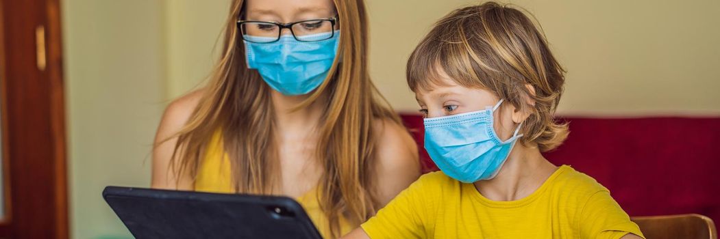 Boy studying online at home using a tablet. Mom helps him learn. Mom and son in medical masks to protect against coronovirus. Studying during quarantine. Global pandemic covid19 virus. BANNER, LONG FORMAT