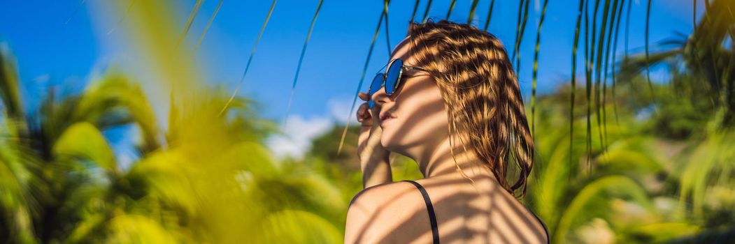 Young woman with the shadow of the palm leaf on her back. Relaxing on the seaside. BANNER, LONG FORMAT