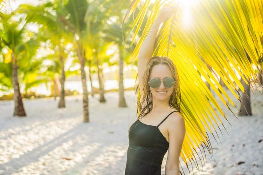 young beautiful woman in swimsuit on tropical beach, summer vacation, palm tree leaf, tanned skin, sand, smiling, happy. Happy traveller woman.