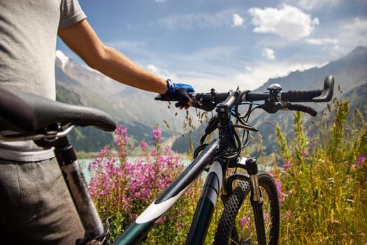 A man stands next to a mountain bike on the background of a mountain lake.