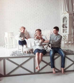 happy parents with five-year-old daughter and their pet dog in the cosy living room