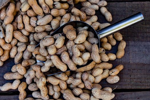 bag and shovel spoon with bulk peanuts on rustic background