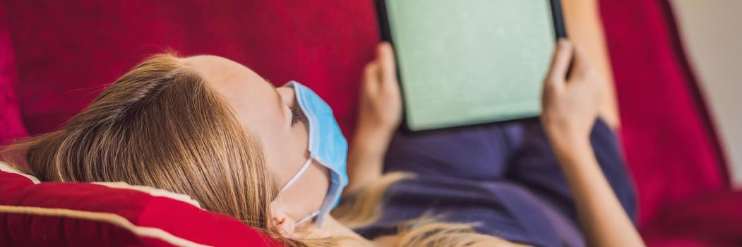 Woman in medical mask reads a book on the couch. Home quarantine. Stay at home. Coronovirus. BANNER, LONG FORMAT