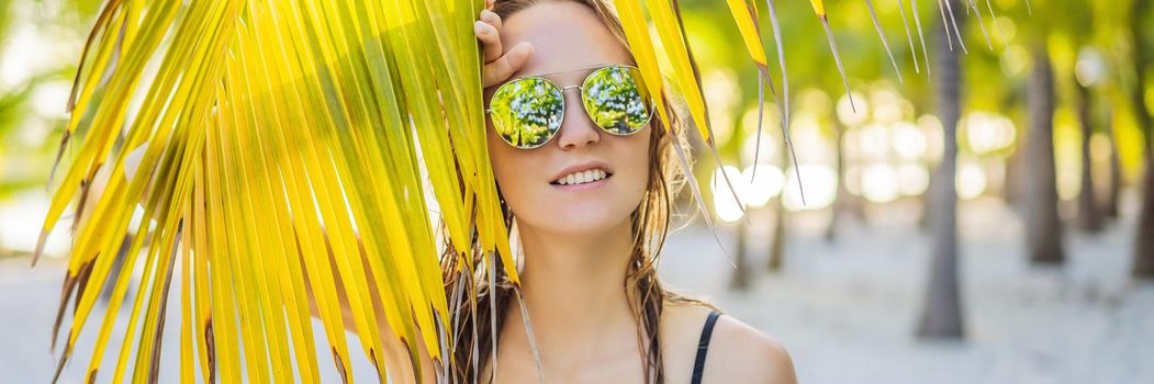 young beautiful woman in swimsuit on tropical beach, summer vacation, palm tree leaf, tanned skin, sand, smiling, happy. Happy traveller woman. BANNER, LONG FORMAT