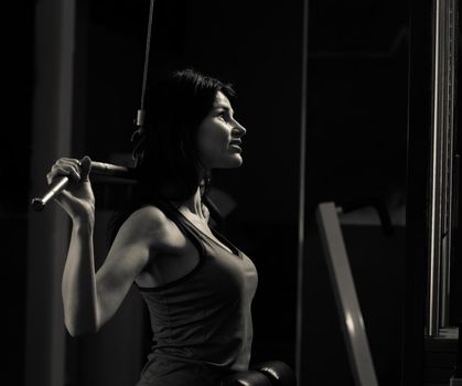 Young business woman doing exercise on a fitness machine in a fitness club. Photo on a dark background.