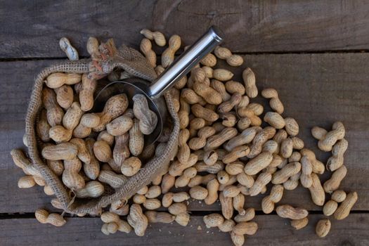 bag and shovel spoon with bulk peanuts on rustic background