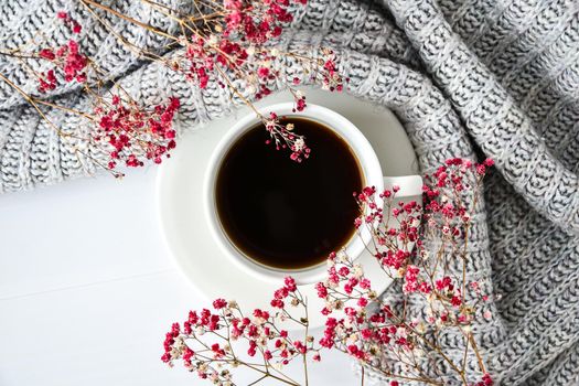 Cup of black coffee on white background with sweater and bright pink flowers. Flat lay. Copy space. Fashion concept. Cozy lifestyle. Still life