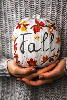 Female hands holding painted pumpkin. Fall decoration. Autumn harvesting. Do it yourself. Thanksgiving concept. Diy. Sweater