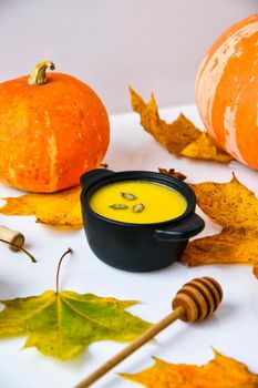 Autumn food. Pumpkin puree soup, leaves. Autumn harvest, pumpkins, leaves on grey as abstract background. Thanksgiving day. Seasonal food. Vegetarian