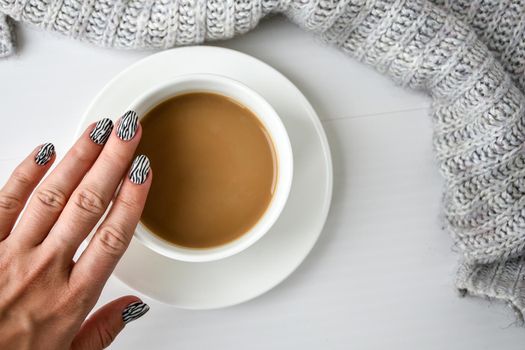 Hand in sweater with zebra animal printed nails with cup of coffee. Female manicure. Glamorous beautiful manicure. Manicure salon concept. Nail polish close up.