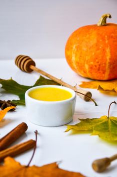 Autumn food. Pumpkin puree soup, leaves. Autumn harvest, pumpkins, leaves on grey as abstract background. Thanksgiving day. Seasonal food. Vegetarian